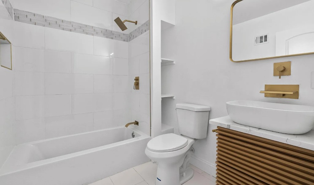 Renovated bathroom with white tile, gold fixtures, and a vessel sink.